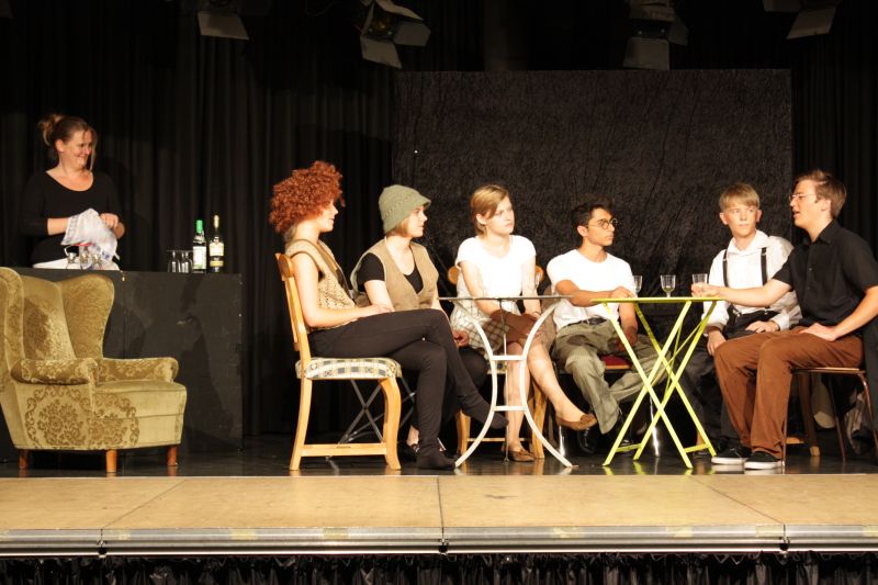 David Shayne (dritter von rechts) im Kreise anderer Literaten, beobachtet von Lehrerin Judith Weyermann in der Rolle der Barfrau. Lisa Herzog (dritte von links) spielt hier eine Autorin. David Shayne (dritter von rechts) im Kreise anderer Literaten, beobachtet von Lehrerin Judith Weyermann in der Rolle der Barfrau. Lisa Herzog (dritte von links) spielt hier eine Autorin.